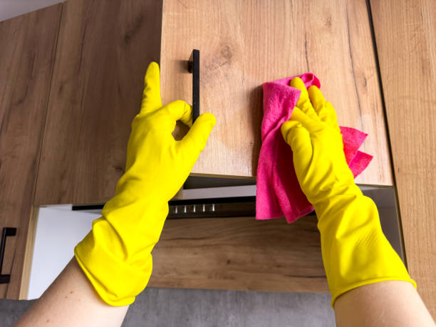 Person wearing yellow gloves cleaning wooden furniture with a pink cloth.