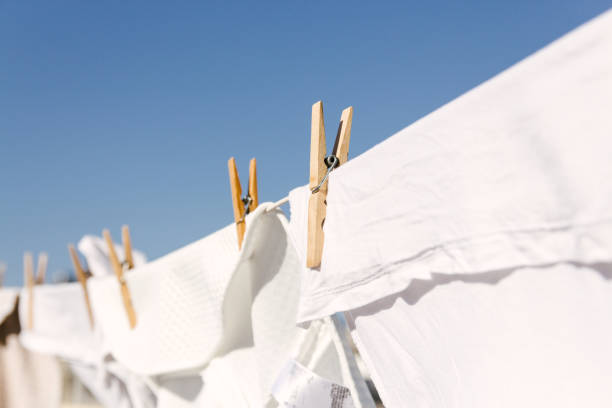 White linens hanging on a clothesline with wooden clothespins against a clear blue sky.