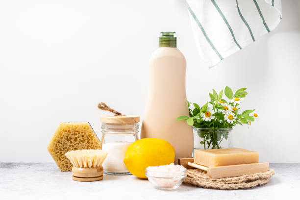 Natural cleaning products including a lemon, soap, a brush, and a jar of baking soda on a counter.