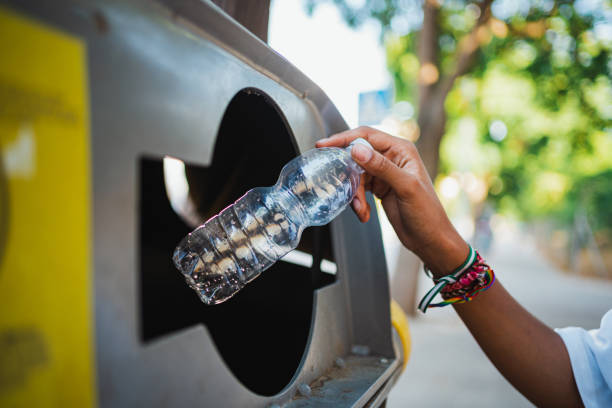 A person discards a plastic bottle into a recycling bin outdoors, illustrating waste management practices.